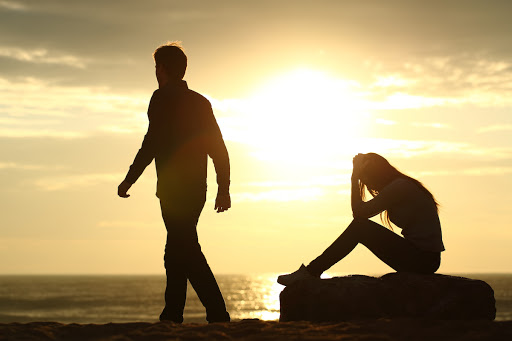 Stel met relatieproblemen bij zonsondergang man loopt weg terwijl vrouw verdrietig zit symbool voor twijfel in relatie.