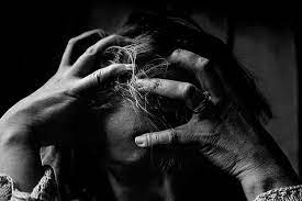 Een zwart-wit foto van een persoon die met beide handen hard in het haar grijpt, hoofd omlaag en zichtbaar in paniek of intense stress. De houding en expressie stralen complete overbelasting uit. De sfeer past bij het gevoel: "Mijn lijf blokkeert alles." Het beeld symboliseert emotionele en fysieke blokkade, innerlijke strijd en totale uitputting